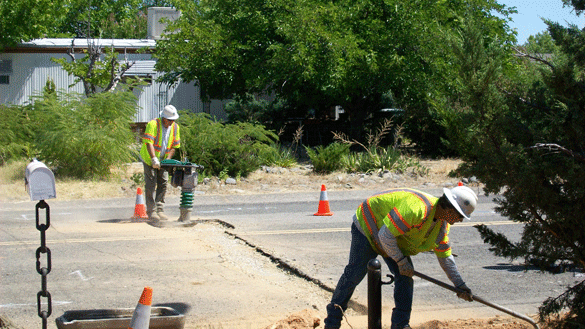 Water Department Leadworker Mike Hartman operates a tamper; Leadworker Andy Diaz works a shovel in the foreground. 