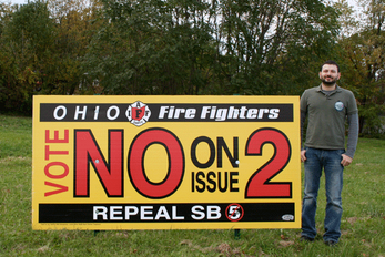Rick Thompson stands next to a Fire Fighters bill board that puts the issue in the clearest possible terms.