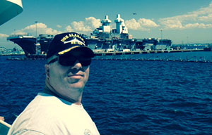 Dan Boschee poses for a photo on the San Diego harbor in front of the USS Boxer amphibious assault carrier